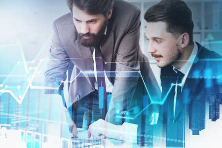 Portrait of two young businessmen working together in blurry city with double exposure of financial...