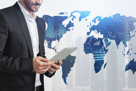Young businessman using tablet in blurry city with double exposure of world map. Toned image.