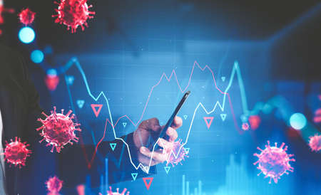 Hand of businessman using smartphone in blurry office with falling graphs and covid 19 coronavirus....