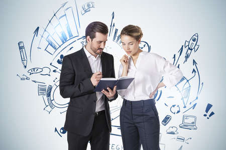 Young businessman and businesswoman working with planner near gray wall with business plan sketch...