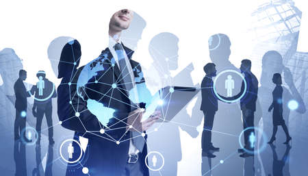 Young businessman standing in blurry office with tablet and his team and double exposure of social network interface. Toned image. Elements of this image furnished by NASAの写真素材