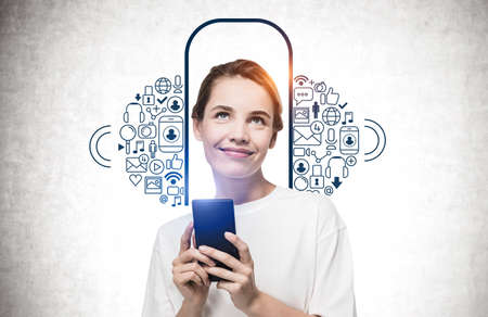 Young woman with smartphone standing near concrete wall with creative social media sketch drawn on...