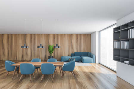 White and wooden hall, blue chairs and table with sofa in the corner near big window. Gray bookshelf...