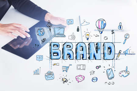 Hands of young businesswoman with tablet in blurry office with double exposure of creative brand sketch. Toned imageの写真素材