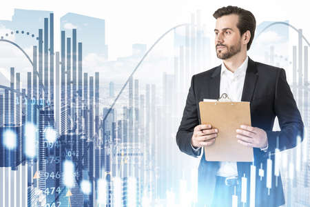 Confident young businessman with clipboard standing in blurry modern city with double exposure of graphs. Toned imageの写真素材