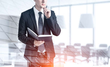 Portrait of thoughtful young businessman with book standing in blurry office. Concept of planning. Toned image double exposureの写真素材