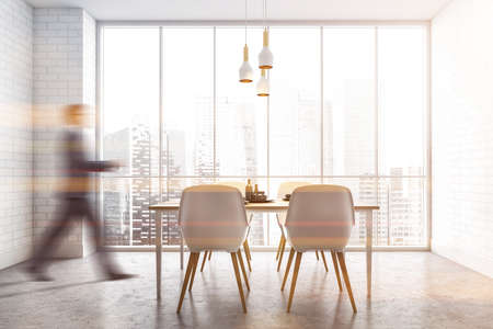 Blurry young man walking in modern dining room with white walls, concrete floor and table with white chairs. Toned imageの写真素材