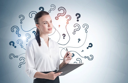 Portrait of serious young woman standing with folder near gray wall with question marks drawn on it. Mock upの写真素材