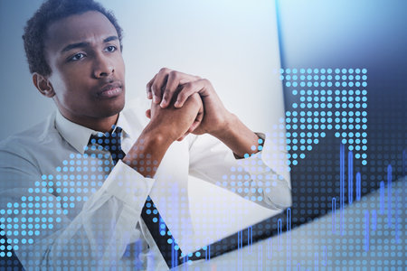 Serious young African American businessman working in blurry office with double exposure of growing...