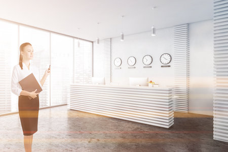Young European businesswoman standing in modern office waiting room with white walls, concrete floor and reception desk. Toned imageの写真素材