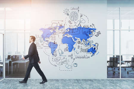 Thoughtful young businessman in formal suit is going throught the white office wall with drawn sketch of colorful global business sketch. Business strategy.の写真素材
