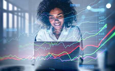 Attractive smiling African American business woman or stock trader analyzing stock graph chart using...
