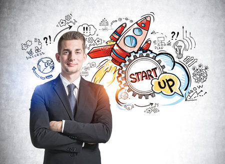 European handsome businessman with crossed arms pose looking at camera and dreaming about launch a business start up and to succeed on it. Concept of success. Colorful rocket sketch drawn on wallの写真素材