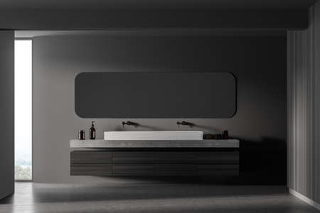 Dark wooden bathroom with two sinks and oval mirror near window. Minimalist gray and dark design of...