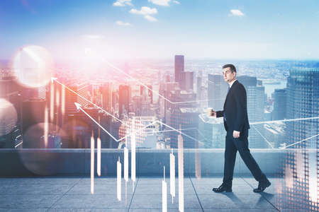 Businessman with graphs, double exposure, walking on the roof of business building, horizon of cityscape. Young man in black suit with coffee. Concept of working in corporationの写真素材