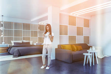 Living room with gray couch, side view, woman standing on marble floor. White coffee tables and dark...