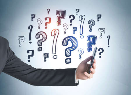 Businessman outstretched hand with smartphone, blue background of doodle question marks drawn on...