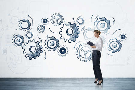 Businesswoman with notebook standing on concrete floor, gears with drawing and lines and arrows. Abstract technical blurred background, technology and engineering. Concept of brainstormの写真素材