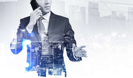 Businessman talking on the phone with hand outstretched, night business buildings, toned image double exposure. Concept of international communication and corporate networkの写真素材