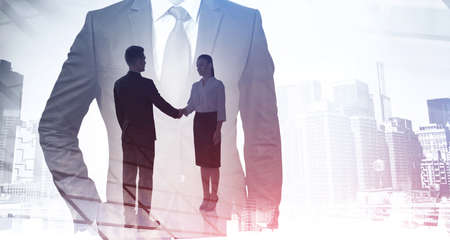 Business people shake hands, double exposure of man in suit and skyscrapers, city buildings toned image. Concept of signing a contract and teamworkの写真素材