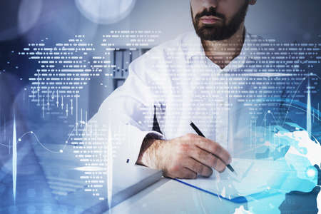 Office man laptop on table, writing in notebook, working in office interior with double exposure of world map and graph dynamics, candlesticks rising. Concept of stock market and financeの写真素材