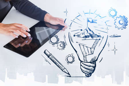 Businesswoman hands fingers touch tablet display, drawing of bulb with mountain top, double exposure with skyscrapers. Concept of new ideas, technology, successの写真素材
