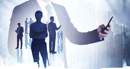 Businessman using smartphone, silhouettes of diverse business people. Double exposure of city skyscrapers, concept of international communication and networkの写真素材