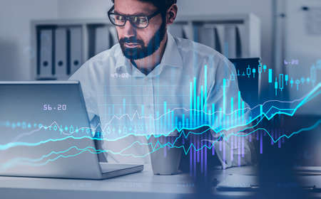 Businessman in eyeglasses analysing stock market changes, sitting in front of the laptop, double...