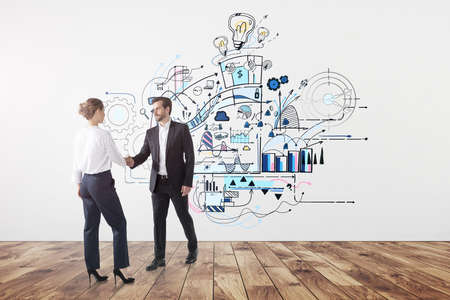 Businessman in suit shakes hands with a businesswoman having an arrangement at empty office with oak wooden floor and sketch on the wall. New ideas give more opportunities for cooperation in businessの写真素材