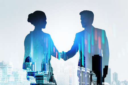 Silhouettes of businessman and businesswoman having a handshake. Panoramic city view in the background. Forex candlestick in the foreground. Concept of networking and cooperation on stock marketの写真素材