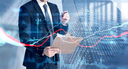 Young businessman is making notes about the situation on the stock market trying to predict its...