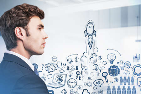 Side view of handsome businessman pondering about start up project. Busines sketch on glass screen. Concept of success and new business project launch.の写真素材