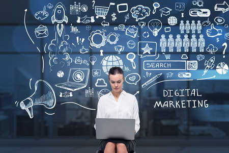 Businesswoman working on laptop and wondering about future perspective in development of digital marketing. Social media icons sketch on background with city view. Concept of success project launch.の写真素材