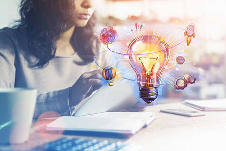 Businesswoman browsing internet via tablet device at office workplace to find new ideas for start up. Colorful light bulb sketch. Concept of creativity and brainstormingの写真素材