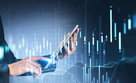 Businesswoman hamds using tablet device with stock market report hologram. Business and financial...