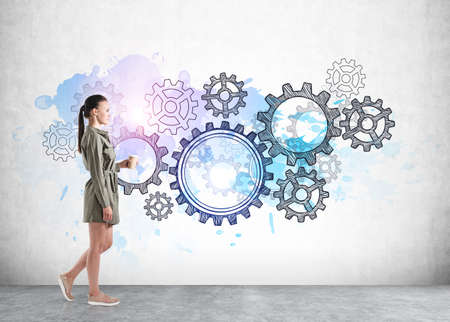 Office woman in green casual dress with coffee. Gray concrete floor and wall with colorful cogwheels and gears doodle. Concept of business workerの写真素材