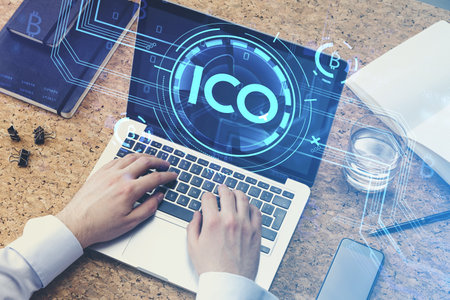 Office man with laptop on table with device and tools, hands typing on keyboard, double exposure with initial coin offering on the screen. Concept of cryptocurrency and bitcoinの写真素材