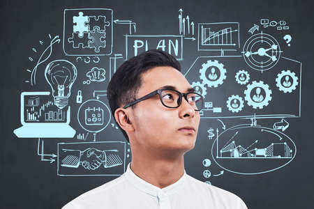 Office asian man in white shirt, looking away. Sketch with business strategy plan on chalkboard,...
