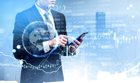 Office man with smartphone, earth hologram and chart with numbers and background of skyscrapers. Double exposure of lines and graphs. Concept of online traderの写真素材