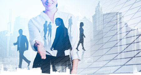 Office woman with extended hand smiling, toned image. Skyscrapers and diverse business partners silhouettes, office buildings double exposure. Concept of agreement and teamの写真素材