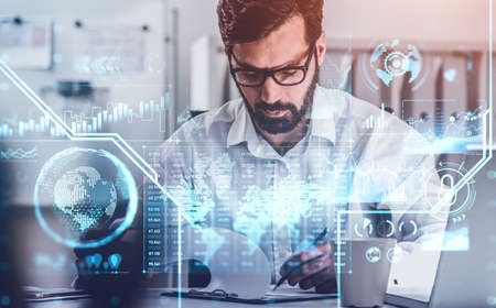 Office man writing a note, beard and eyeglasses. Blue hologram of digital interface with bar chart...