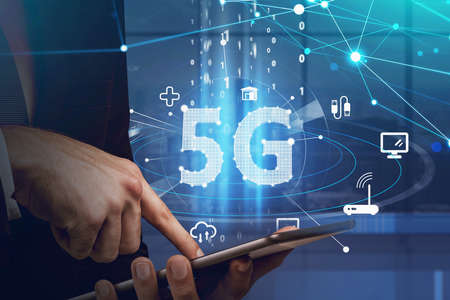 Businessman working with tablet device and browsing the Internet using touch screen. Blue hologram icons of 5G digital network. Wireless systems and high speed signalの写真素材