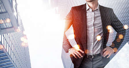 Confident businessman with hands on waist, looking for approaches to tasks solutions. Low angle New York panoramic city view at sunset. Business development concept. Double exposureの写真素材