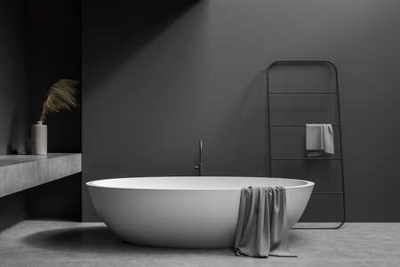 Dark gray bathroom with concrete floor, oval white ceramic bathtub and easy hanger, tied in the minimalistic interior design. 3d renderingの写真素材