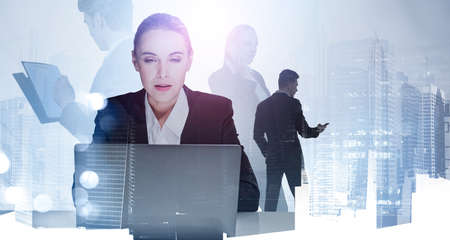 Portrait of concentrated attractive woman analyst who is carrying out a research on laptop. Double exposure. New York cityscape. Silhouettes of colleaguesの写真素材
