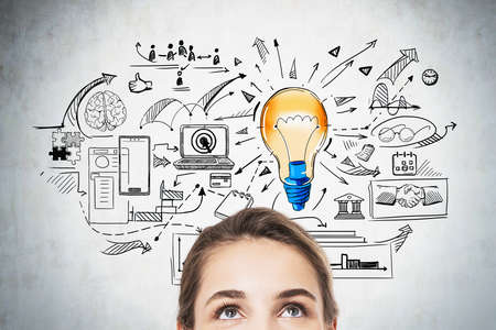 Half portrait of businesswoman looking up at colorful lightbulb and business sketches on concrete...