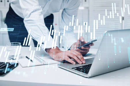 Businessman trader is using laptop to continue trading operations and checking quotes in smartphone....