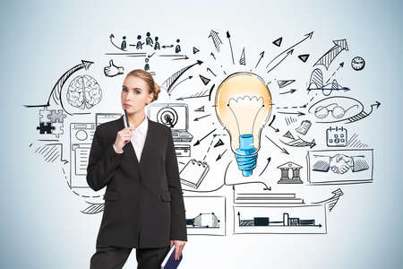 Front view businesswoman in formal wear holding a pen on chin and pondering about start up solutions holding a book on hand, blue wall with colorful light bulb and business flowchart sketchesの写真素材