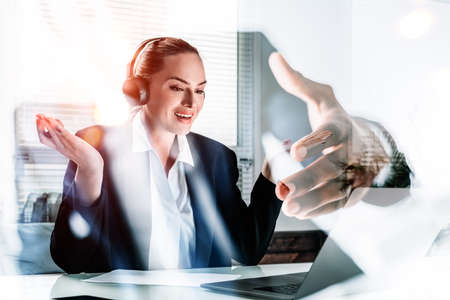 Businesswoman wearing formal suit is sitting at workplace inside the office in front of the laptop listening the podcast via headphones. Concept of cooperation and communication using gadgetsの写真素材