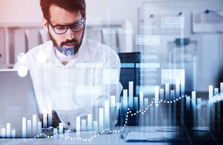 Businessman wearing formal suit is sitting at workplace working on the laptop analyzing stock market...
